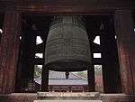 A large bronze bell with cross design hanging in an open roofed belfry.