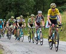 A group of cyclists riding up an incline being led by a one wearing a yellow jersey.