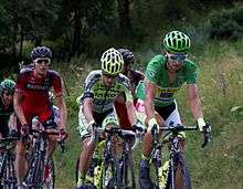 A group of cyclists riding up an incline being lead by one wearing a green jersey.