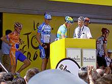 A group of cyclists on a stage near a podium.
