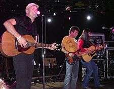 Three man on stage playing three different guitars.