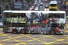 A bus with Optimus Prime and Chinese characters printed on its side drives across a street.