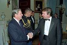 Trump shaking hands with President Ronald Reagan in 1987. Both are standing and facing each other.