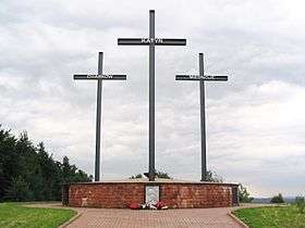 A memorial consisting of three crosses standing on a large brick pedestal. Each cross bears a name – Katyn, Kharkiv, or Mednoye.