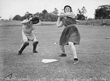 Black-and-white photo with a baseball catcher crouching behind the plate while a female batter gets ready for a pitch