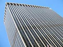 Street view of top half of skyscraper against the sky; its outside is dominated by vertical black and white lines