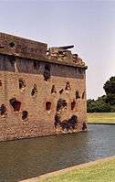 behind a water-filled moat, Fort Pulaski’s brick masonry wall is pot-marked with cannonball strikes.