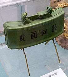 A green plastic-bodied mine supported by a pair of scissor legs, with the text "此面向敌" (this side towards enemy) on the front.
