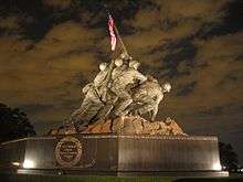 Color photo of the Marine Corps War Memorial, a bronze statue of six Marines raising a U.S. flag attached unto a Japanese pipe atop Mount Suribachi
