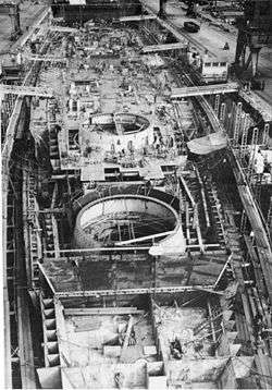 Black and white photograph of a ship under construction. The ship has not been fitted with its deck, and there are three large circular holes in the superstructure visible.