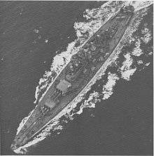 A large battleship steams through choppy seas. Three floatplanes are located on the stern.