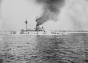 Black-and-white photo of a ship with a single funnel sailing to the left.