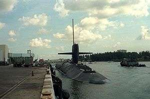 Submarine moored in pier, next to a moving tug.