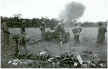 Soldiers operating a field gun. A large cloud of smoke is coming from the barrel while there is a pile of used shells to the rear