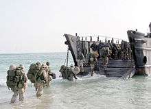 Colour photograph of marines wading into an amphibious landing craft.