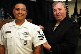 Rear admiral Terry McCreary presenting a rating insignia of a Mass Communication Specialist First Class (MC1).