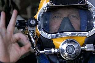 A diver touches his first finger tip to his thumb tip while extending his other fingers