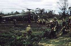 A group of Marines carry a wounded Marine to a helicopter.