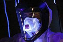 A person wearing full protective gear, glowing in ultraviolet light