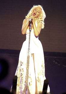  A blond woman dressed in white singing to a microphone.