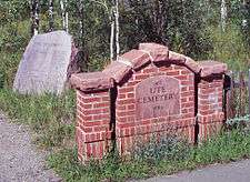 A small arched brick structure capped with stone. Set in the middle is a stone tablet with "Ute Cemetery, 1880" carved in it. Behind it to the left is a stone with "Civil War Veterans" and a list of named carved below.