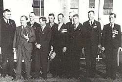 A group of ten men wearing suits and military medals gathered together outside of a building.