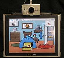 A screen showing a stylised version of a bedroom, mounted on top of the screen is the sensor for a head mouse