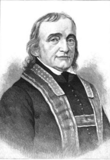 Black and white portrait photograph from the waist up of a man with almost-shoulder-length hair wearing a stole