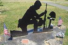 A metal cutout 2-D sculpture of a soldier kneeling at the grave of a fallen comrade.