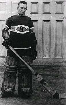 An ice hockey Goaltender stands, also wearing a Canadians jersey, small leg pads and old style gloves, he also is without a mask, while posing for the photo but it was also the style of the time.