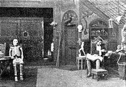 Victor Frankenstein, seated in his laboratory, gesturing towards a skull held in his other hand