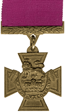A medal in the shape of a cross hanging from a crimson red ribbon.