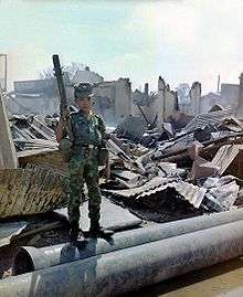 A young child, 12, in uniform with a grenade launcher standing in rubble
