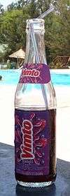 a bottle of Vimto with a straw placed on a table near a swimming pool on a sunny day