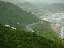 Aerial view of two-lane highway, surrounded by forest and beach