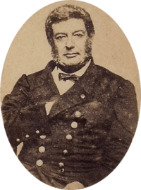 Photographic portrait of a dark-haired man with sideburns, dressed in a double-breasted military tunic with his right hand tucked under the lapel of his jacket
