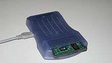 Photo of a blue colored device with a large slot in front, and a cable is attached to the device