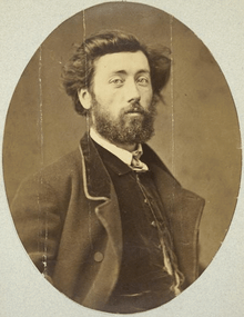 Chest-high portrait of man in his twenties with brown eyes and dark medium-long hair and a beard, wearing a vest and suitcoat and white shirt