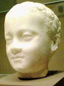  Three-quarter view of a sculpture of a young child's head, the child appears smiling his face has relaxed expressions as he gazes over the viewer's shoulders