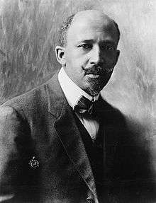 A dignified African-American man, with a mustache, dressed stylishly, sitting down.