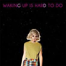 A woman in a blonde wig standing against a star-lit black background. Block pink text above reads "Waking Up is Hard to Do."