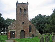 A brick church with its tower at the east end; this contains a round-headed doorway, an oval window, twin bell openings, and simple pinnacles
