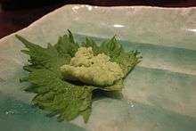 Dab of wasabi on a green shiso leaf, possibly at a sushi-bar counter