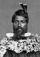 Man wearing traditional Māori cloak with two feathers in his hair