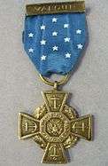 Front of a bronze cross-shaped medal hanging from a blue ribbon