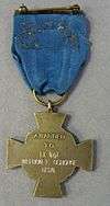 Back of a bronze cross-shaped medal hanging from a blue ribbon