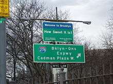 Rectangular blue-and-green sign reading, "Welcome to Brooklyn. How sweet it is!"