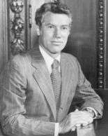 A man, in a business suit, sitting, facing the camera.