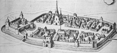 A city is surrounded by a thick, crenelated wall; on one end of the city stands the citadel, which itself is surrounded by a thick wall and has a single entry; in the center of the city stands a church with a tall spire. The city is surrounded by a moat.