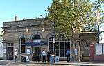 A beige-bricked building with a rectangular, dark blue sign reading "WEST BROMPTON STATION" in white letters all under a light blue sky